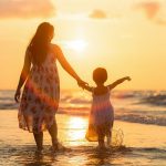 Une mère et sa fille marchant sur la plage au coucher du soleil.