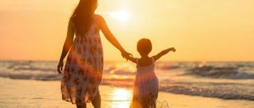 Une mère et sa fille marchant sur la plage au coucher du soleil.