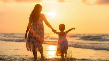 Une mère et sa fille marchant sur la plage au coucher du soleil.