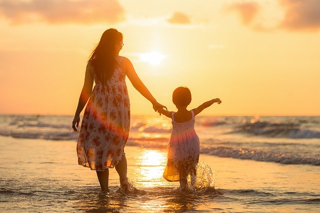 Une mère et sa fille marchant sur la plage au coucher du soleil.