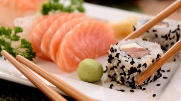 Une assiette blanche avec sushi, sashimi et baguettes.