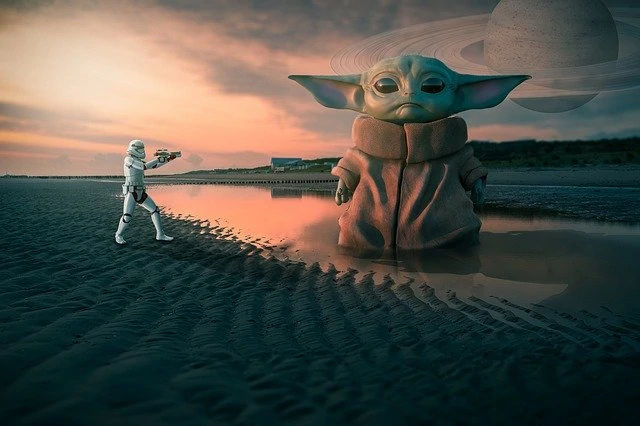 Un bébé Yoda se tient sur la plage à côté d’une planète.
