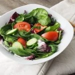 Un bol de salade d'épinards avec tomates et concombres.