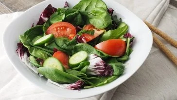 Un bol de salade d'épinards avec tomates et concombres.