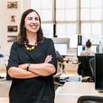 Une femme debout dans un bureau, les bras croisés.