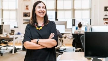 Une femme debout dans un bureau, les bras croisés.