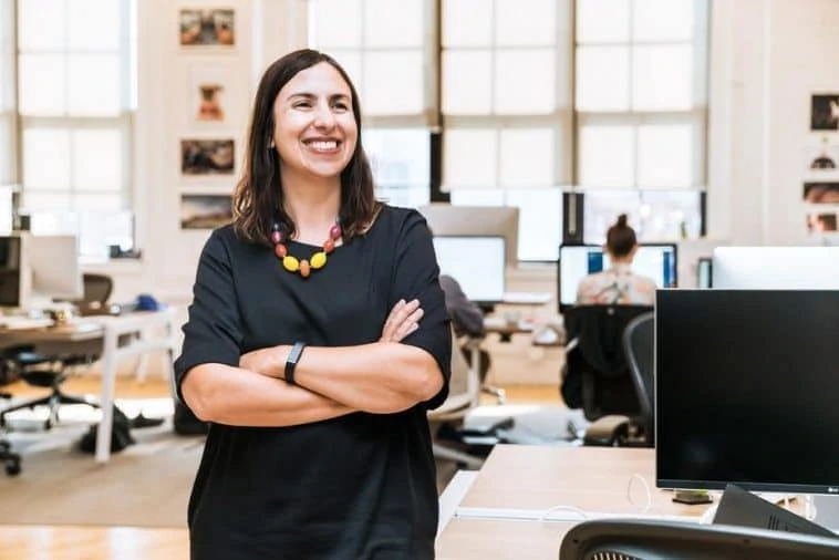 Une femme debout dans un bureau, les bras croisés.