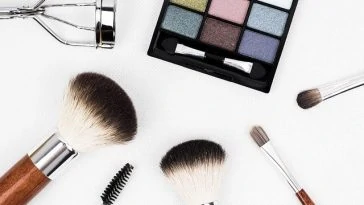 Une variété de pinceaux de maquillage et de produits cosmétiques sont disposés sur une surface blanche.