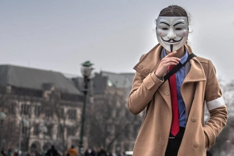 Un homme en trench-coat et cravate portant un masque v pour vendetta.