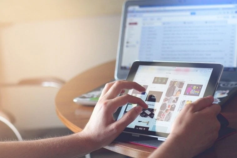 Une personne utilisant un iPad sur un bureau avec un ordinateur portable.