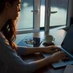 Une femme travaillant sur son ordinateur portable devant une fenêtre.