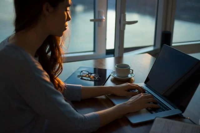 Une femme travaillant sur son ordinateur portable devant une fenêtre.