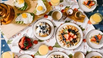 Petit-déjeuner avec gaufres, œufs et fruits sur une nappe.