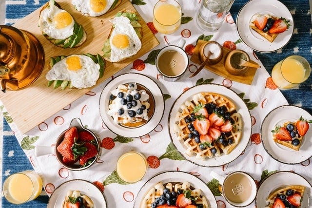 Petit-déjeuner avec gaufres, œufs et fruits sur une nappe.