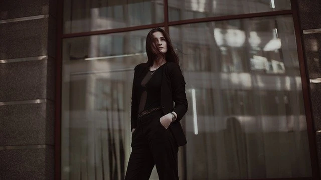 Une femme en costume noir debout devant une fenêtre.