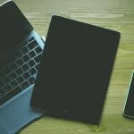 Une table en bois présentant un ordinateur portable, une tablette et un téléphone.