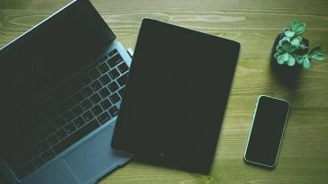 Une table en bois présentant un ordinateur portable, une tablette et un téléphone.