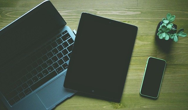 Une table en bois présentant un ordinateur portable, une tablette et un téléphone.