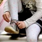 Une petite fille attache ses chaussures sur un banc.