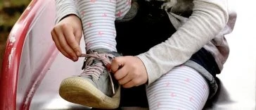 Une petite fille attache ses chaussures sur un banc.