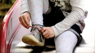 Une petite fille attache ses chaussures sur un banc.