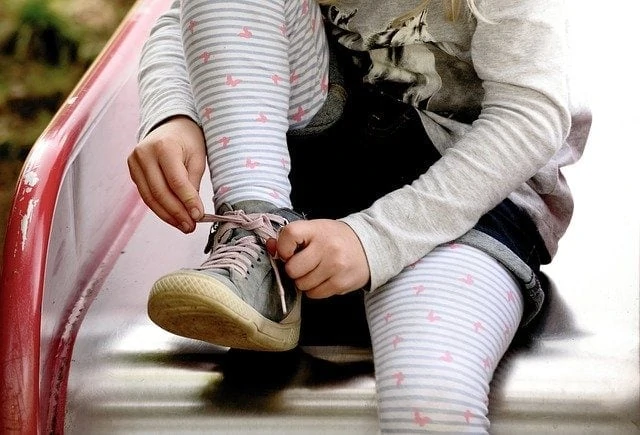 Une petite fille attache ses chaussures sur un banc.