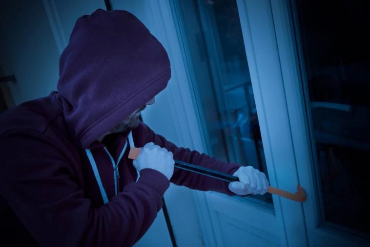 Un cambrioleur en sweat à capuche ouvre une porte avec un couteau à Paris.