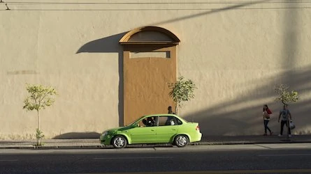 Une voiture verte est garée devant un immeuble.
