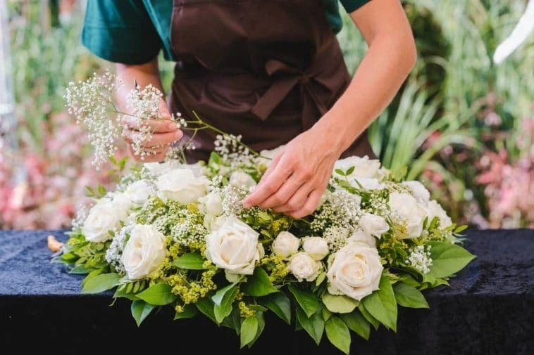 Un fleuriste arrange des roses blanches sur une table.