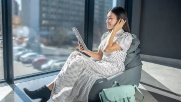 Une femme assise sur un fauteuil poire avec une tablette parcourant des conseils de mode.