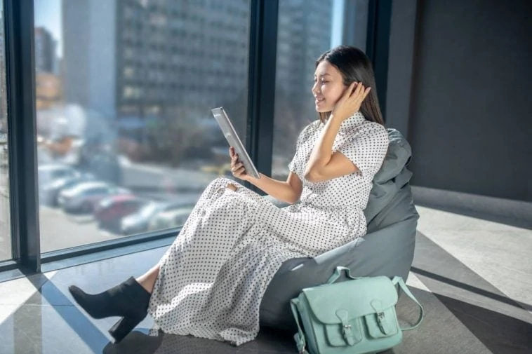 Une femme assise sur un fauteuil poire avec une tablette parcourant des conseils de mode.