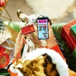 Une femme en bonnet de Noël est assise sur un canapé avec des cadeaux.