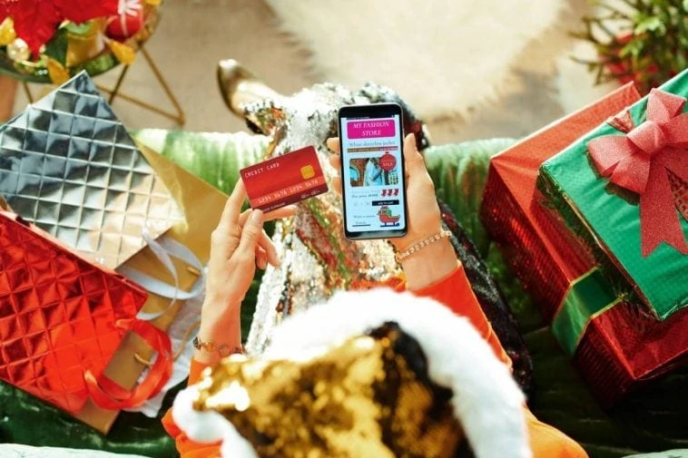 Une femme en bonnet de Noël est assise sur un canapé avec des cadeaux.