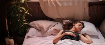 Une femme dormant dans un lit à côté d’une fenêtre.
