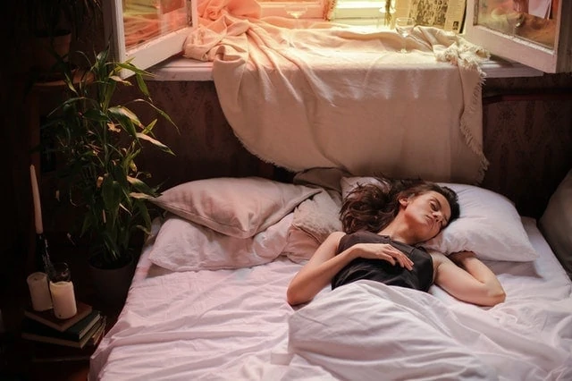 Une femme dormant dans un lit à côté d’une fenêtre.