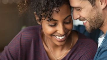 Un couple se sourit tout en regardant un ordinateur portable, mettant en valeur l'amour et l'authenticité.