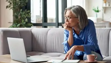 Une femme âgée comparant un écran industriel et un écran domestique, assise sur un canapé.