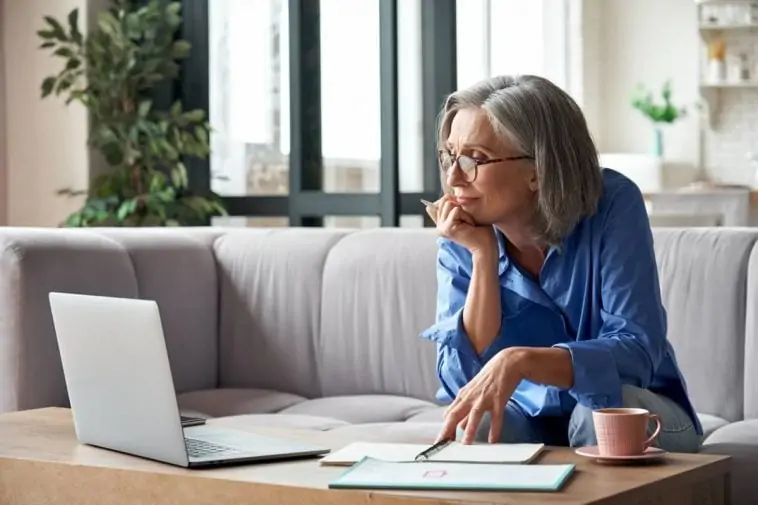 Une femme âgée comparant un écran industriel et un écran domestique, assise sur un canapé.