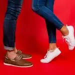Un homme et une femme portent des pantalons à la mode et des chaussures blanches, debout sur un fond rouge.