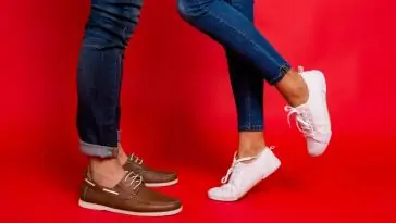 Un homme et une femme portent des pantalons à la mode et des chaussures blanches, debout sur un fond rouge.