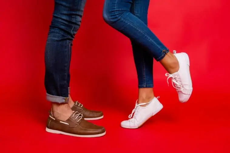 Un homme et une femme portent des pantalons à la mode et des chaussures blanches, debout sur un fond rouge.