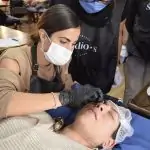 Une femme se fait coiffer les sourcils par un homme masqué.