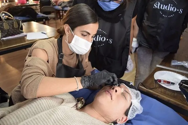 Une femme se fait coiffer les sourcils par un homme masqué.