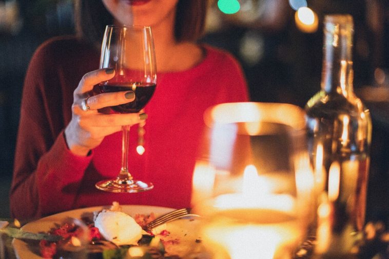 Une femme tient un verre de vin dans un restaurant. L'étiquette à table