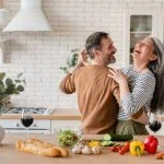 Un couple rit dans la cuisine tout en préparant à manger pour célébrer son anniversaire de mariage.