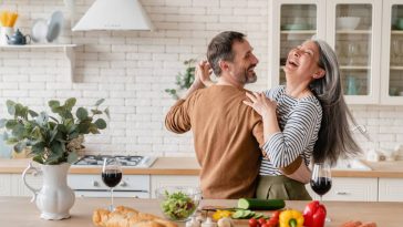 Un couple rit dans la cuisine tout en préparant à manger pour célébrer son anniversaire de mariage.