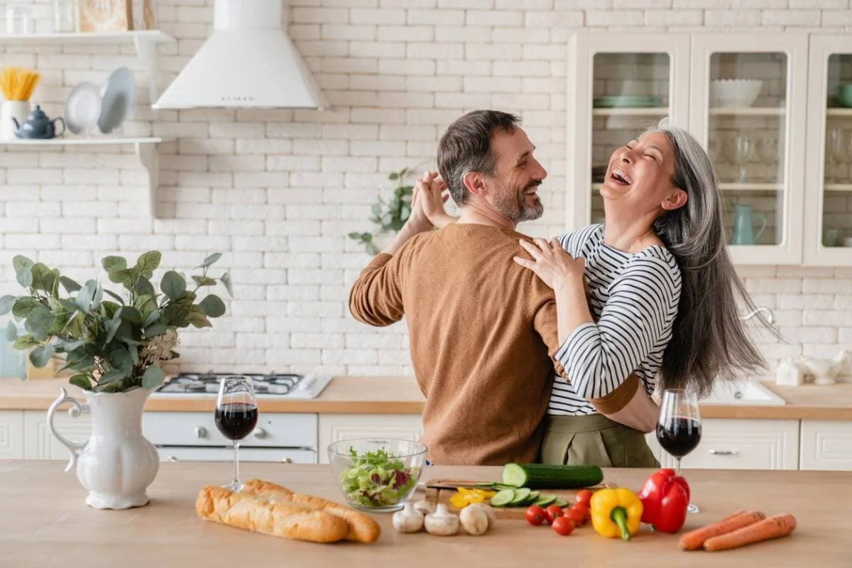 Un couple rit dans la cuisine tout en préparant à manger pour célébrer son anniversaire de mariage.