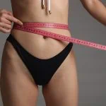 Une femme en bikini mesurant sa taille avec un ruban à mesurer.