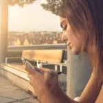 Une femme assise sur un banc regarde son téléphone.