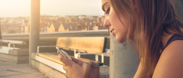 Une femme assise sur un banc regarde son téléphone.